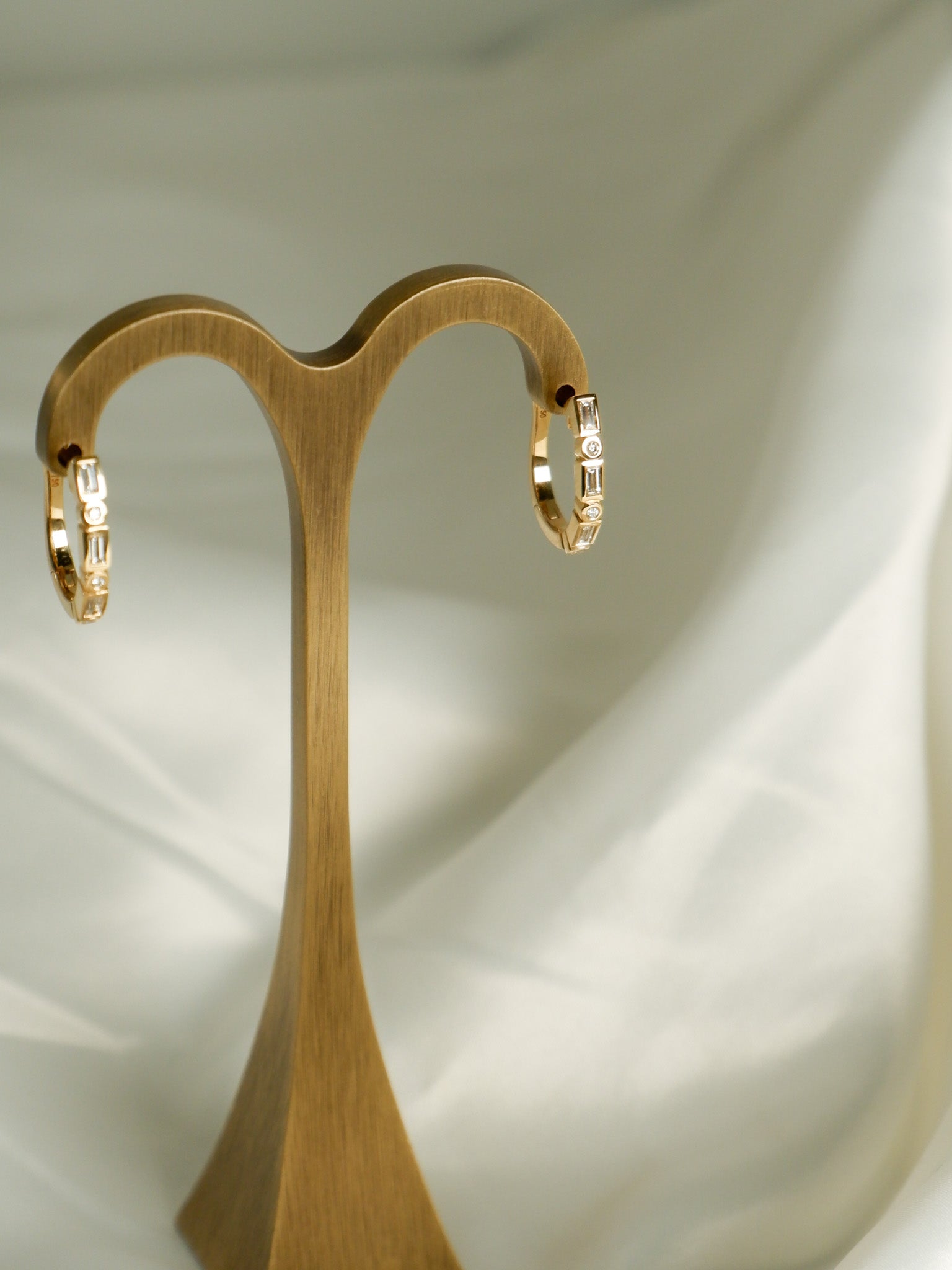 Wooden earring stand holding A.G Designer Jeweller signature bezel set diamond huggie earrings in yellow gold.