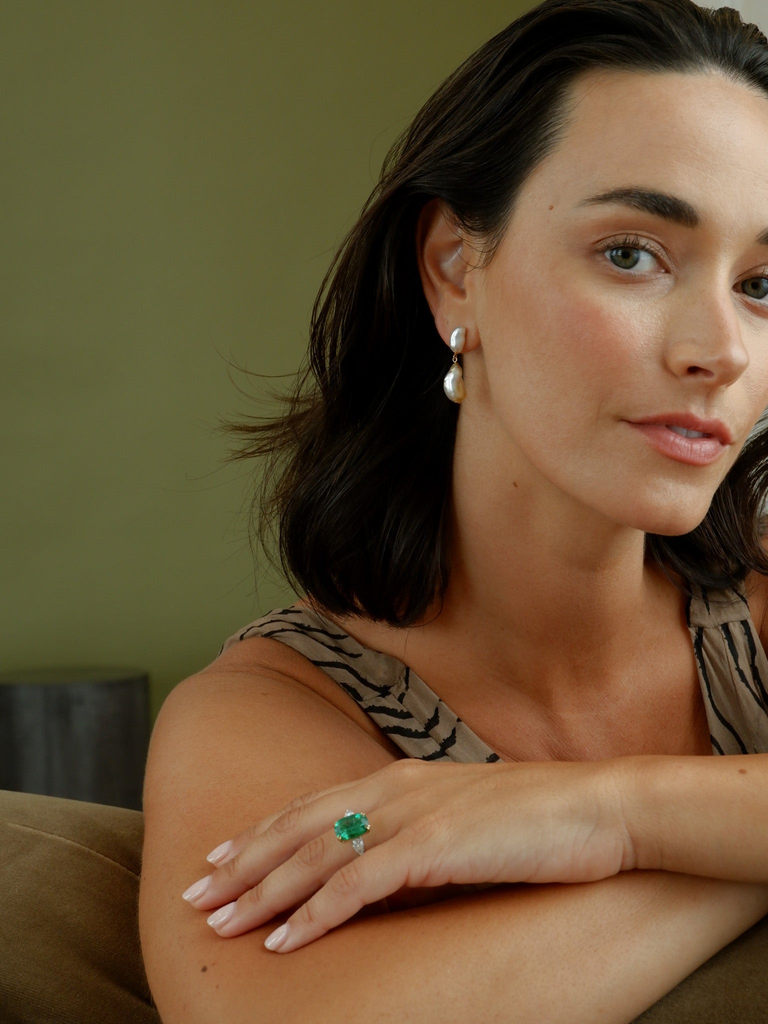 Woman with arms folded, with A.G Cushion Cut Emerald with Pear Cut Diamonds ring on her finger.