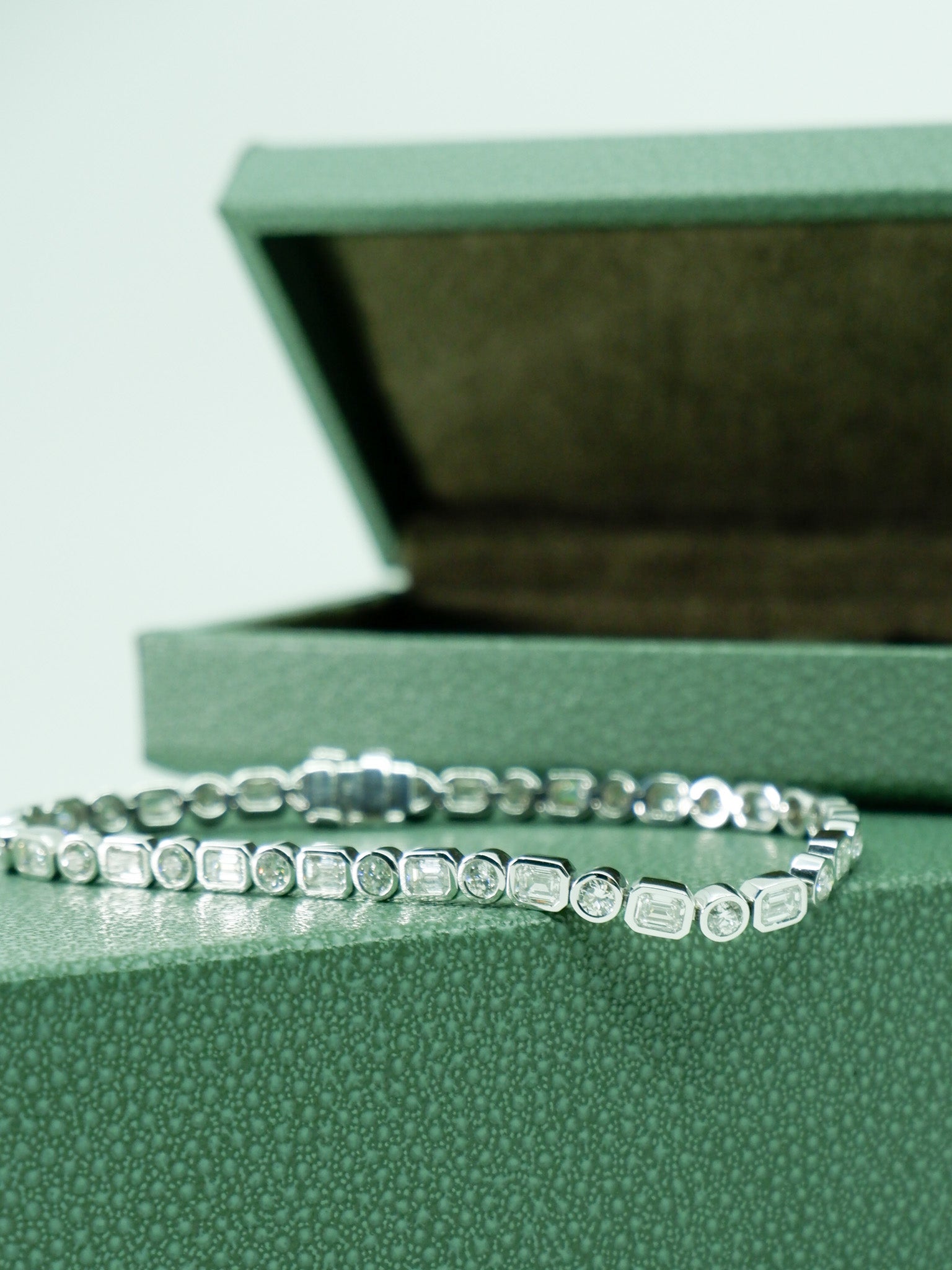 A.G Designer Jeweller custom made alternating round brilliant cut and emerald cut diamond tennis bracelet sitting on green jewellery box.
