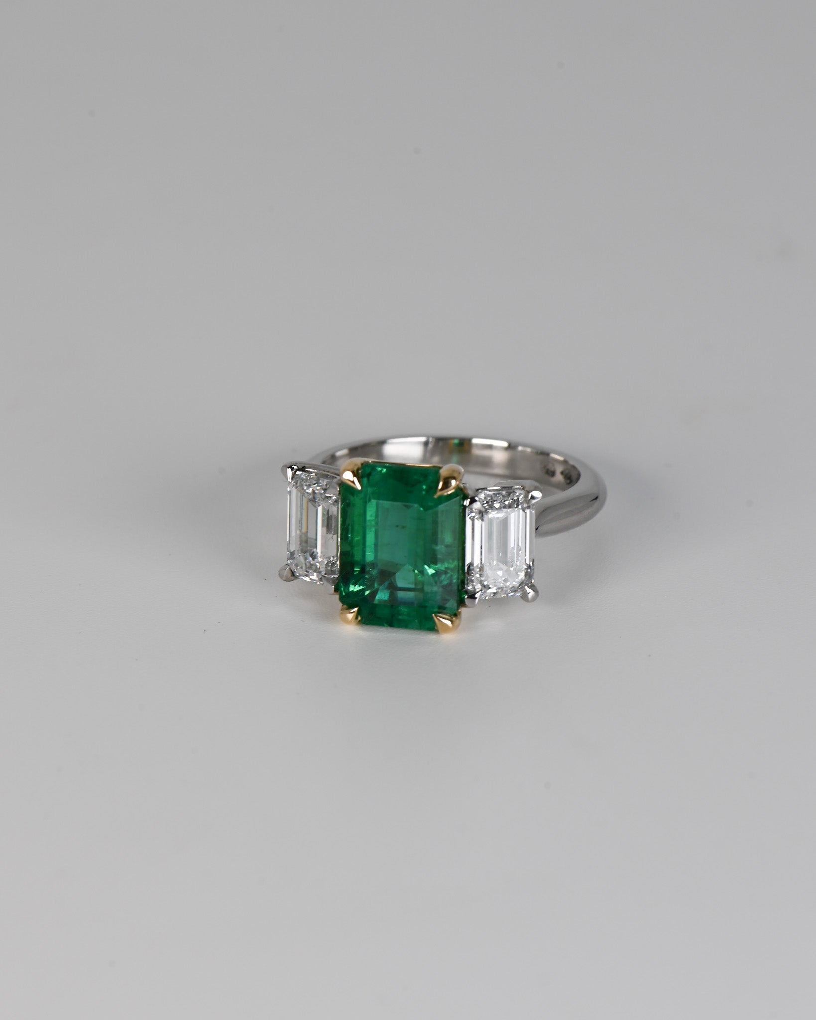 Emerald and diamond trilogy ring on white background.