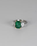 Emerald and diamond trilogy ring on white background.