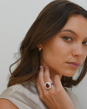 Close up of woman touching neck. Hand has A.G 9.75ct oval cut spessartite garnet and diamond ring on fingre.