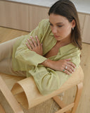 Woman in green top lounging in chair with arms crossed and oval emerald ring on pinky finger.