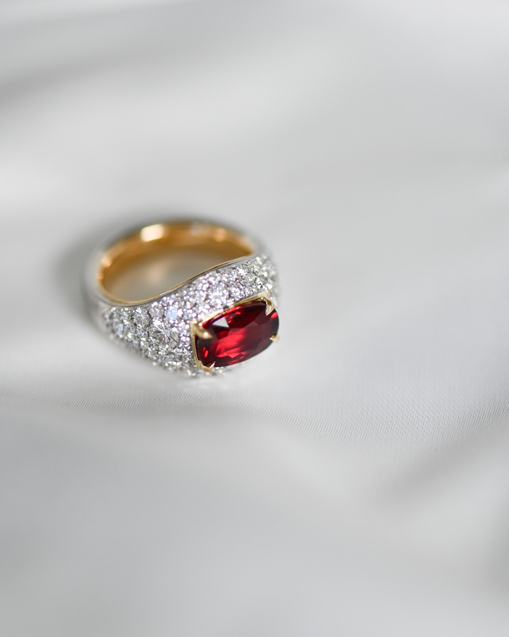 Close up of A.G custom random pave diamond and Ruby on white satin sheet.